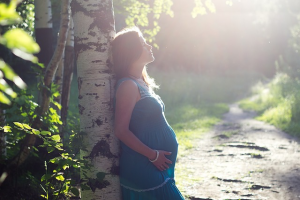 Gravid kvinde læner sig op af et træ